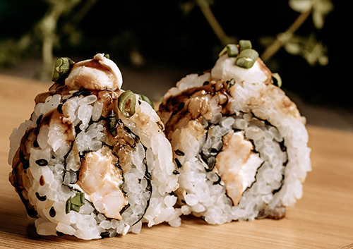 Sushi World Insight Cover page. Two sushi rolls on a wooden board with chopsticks beside them. The background is blurred, showing greenery and a dark ceramic object.